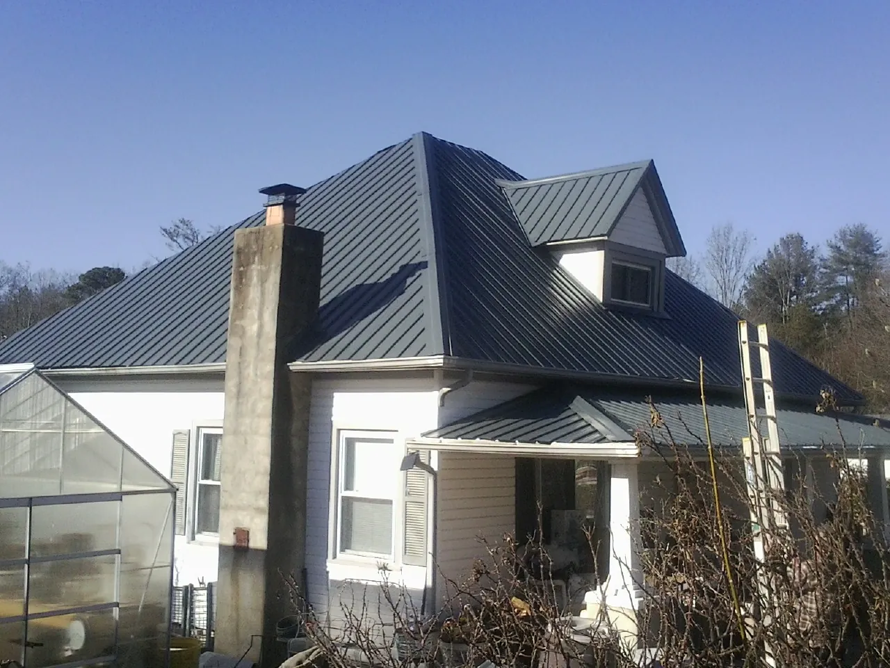 Dark blue standing seam metal roof on a white farmhouse with dormer — Slate & Tile Roof Repair by Roofing Brothers in Bradner