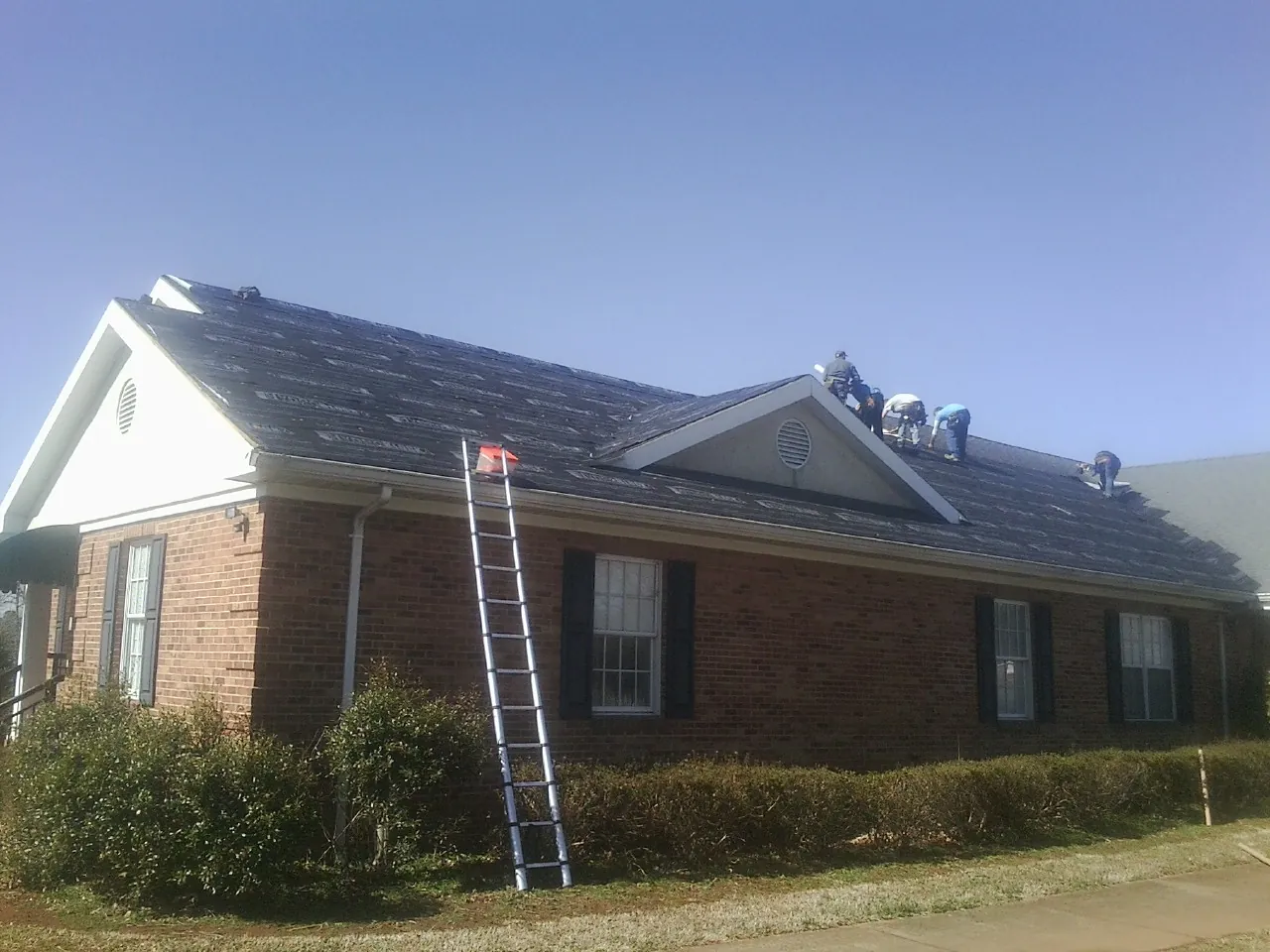Crew tearing shingles off a brick ranch roof with a ladder set — Emergency Roof Repair work by our crew in Bradner
