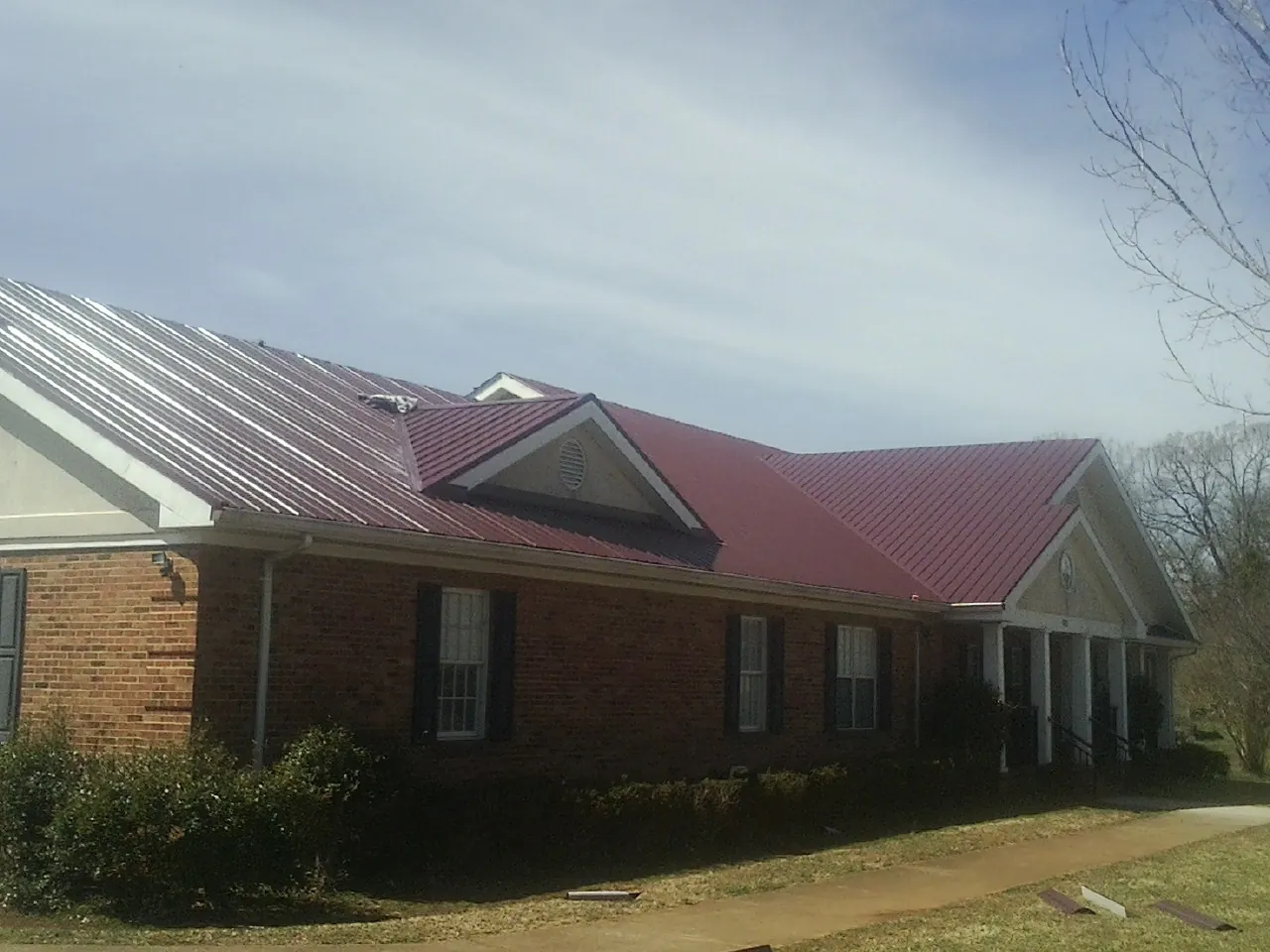 Red metal roof with gabled entries on a long brick building, from a Hail Damage Roof Repair job in Bradner