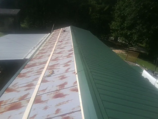 Old rusted panels beside newly installed green metal roofing — Wind Damage Roof Repair by Roofing Brothers in Bradner