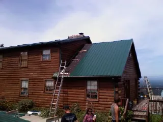 Green metal roof going on a two story log home with ladders set in Bradner
