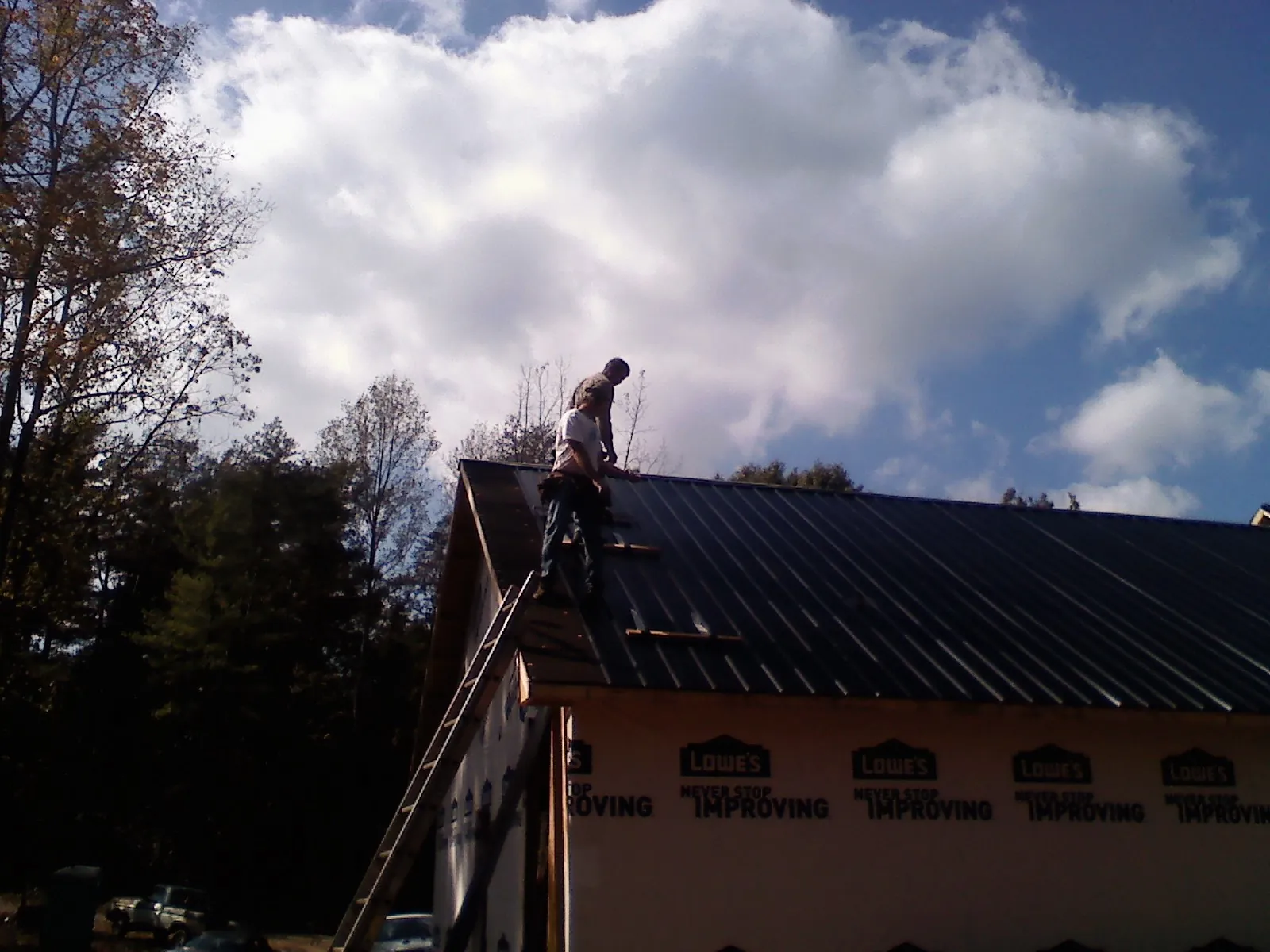 Roofer fastening dark metal panels high against a cloudy sky, from a Roof Inspection job in Bradner